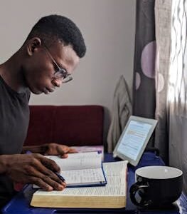 Young man deeply immersed in reading and studying with books and tablet.