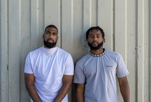 Two young men standing against a gray wall, exuding casual style and friendship vibes.